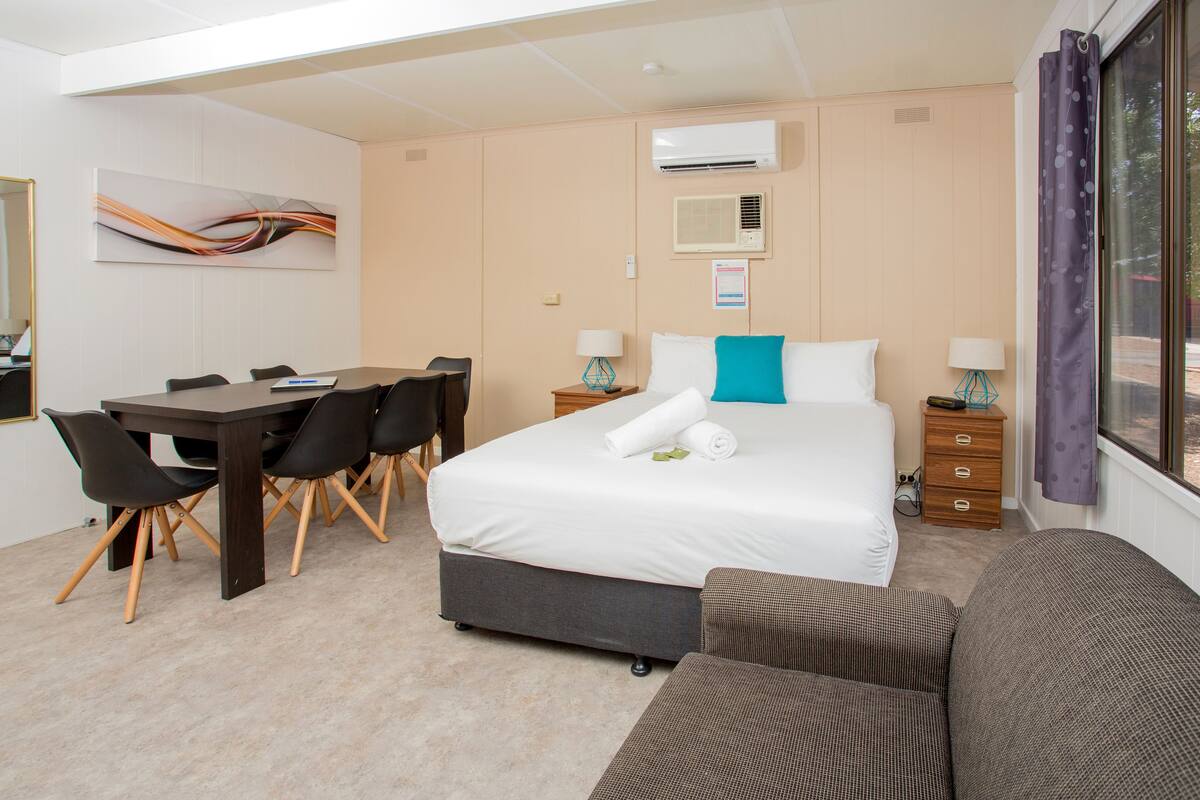 A hotel room with a bed, a desk, chairs, a sofa, and a window with curtains.