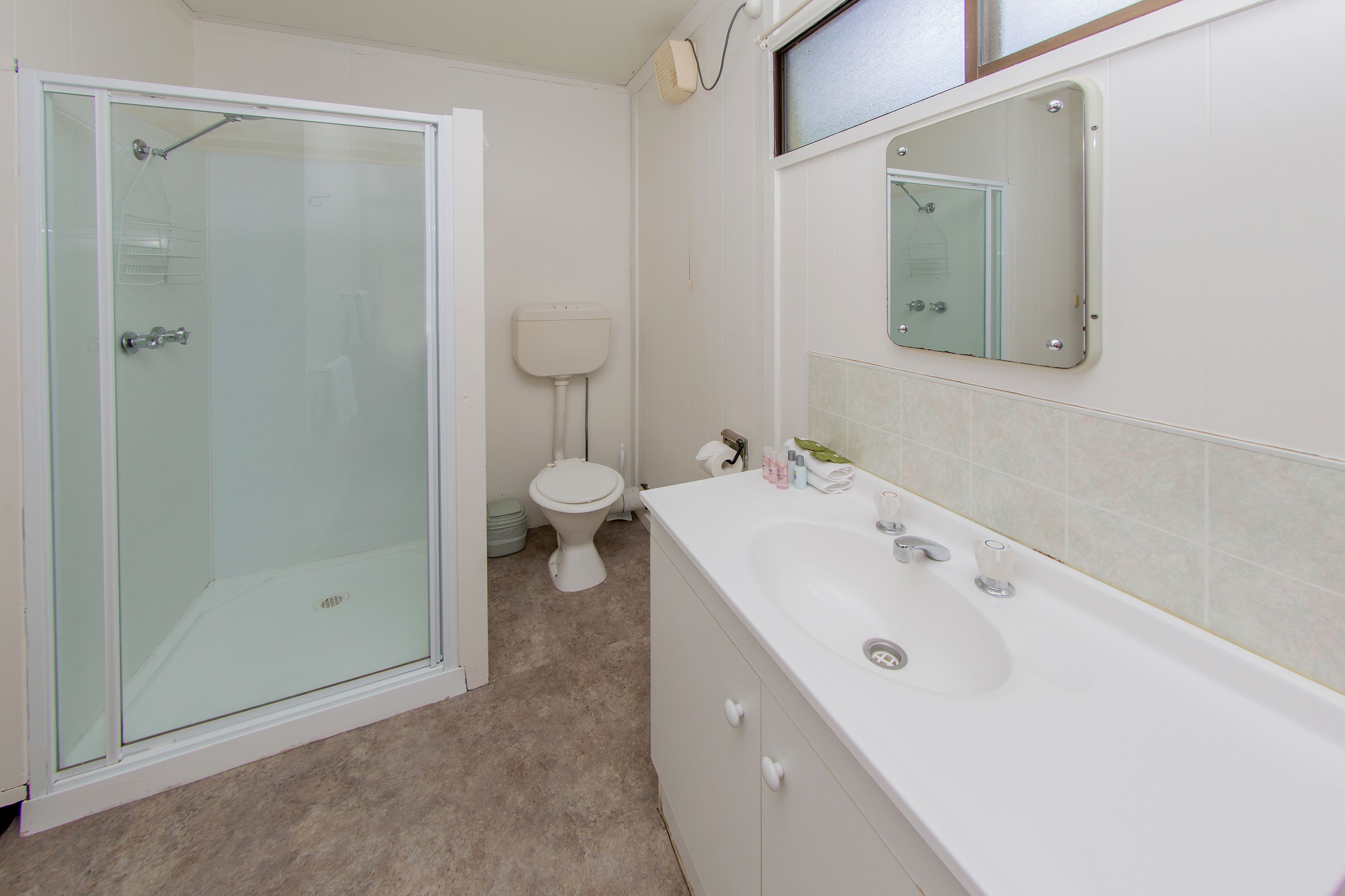 Un baño con ducha acristalada, inodoro y lavamanos con espejo.