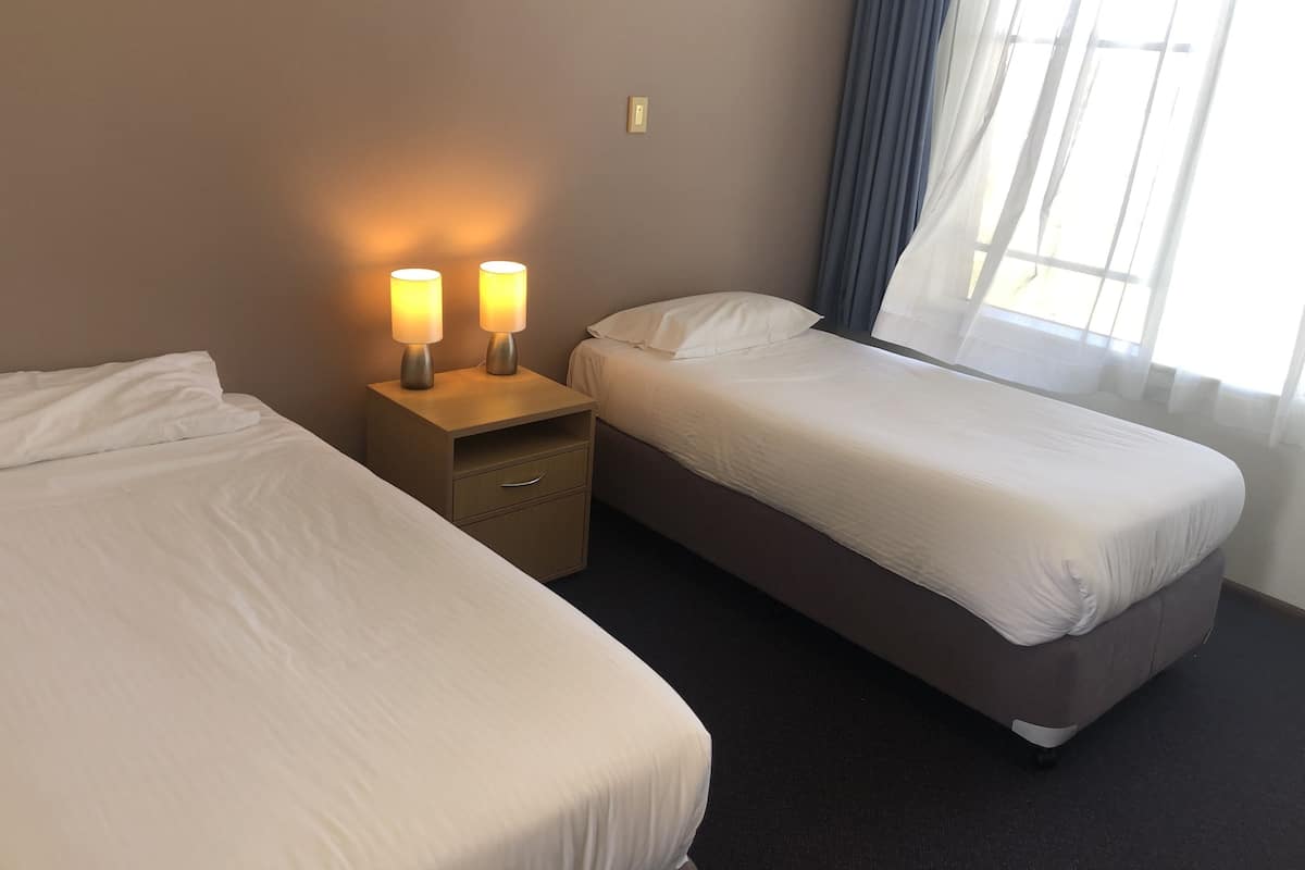 A hotel room with two beds, a nightstand with lamps, a small drawer, and a window with curtains.