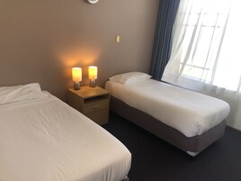 Una habitación de hotel con dos camas individuales, una mesita de noche con dos lámparas, un cajón pequeño y una ventana con cortinas.
