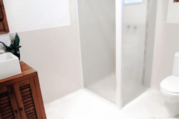 A modern bathroom with a glass-enclosed shower, a white sink, and a toilet. - Vanuatu Beachfront Apartments (Mele)