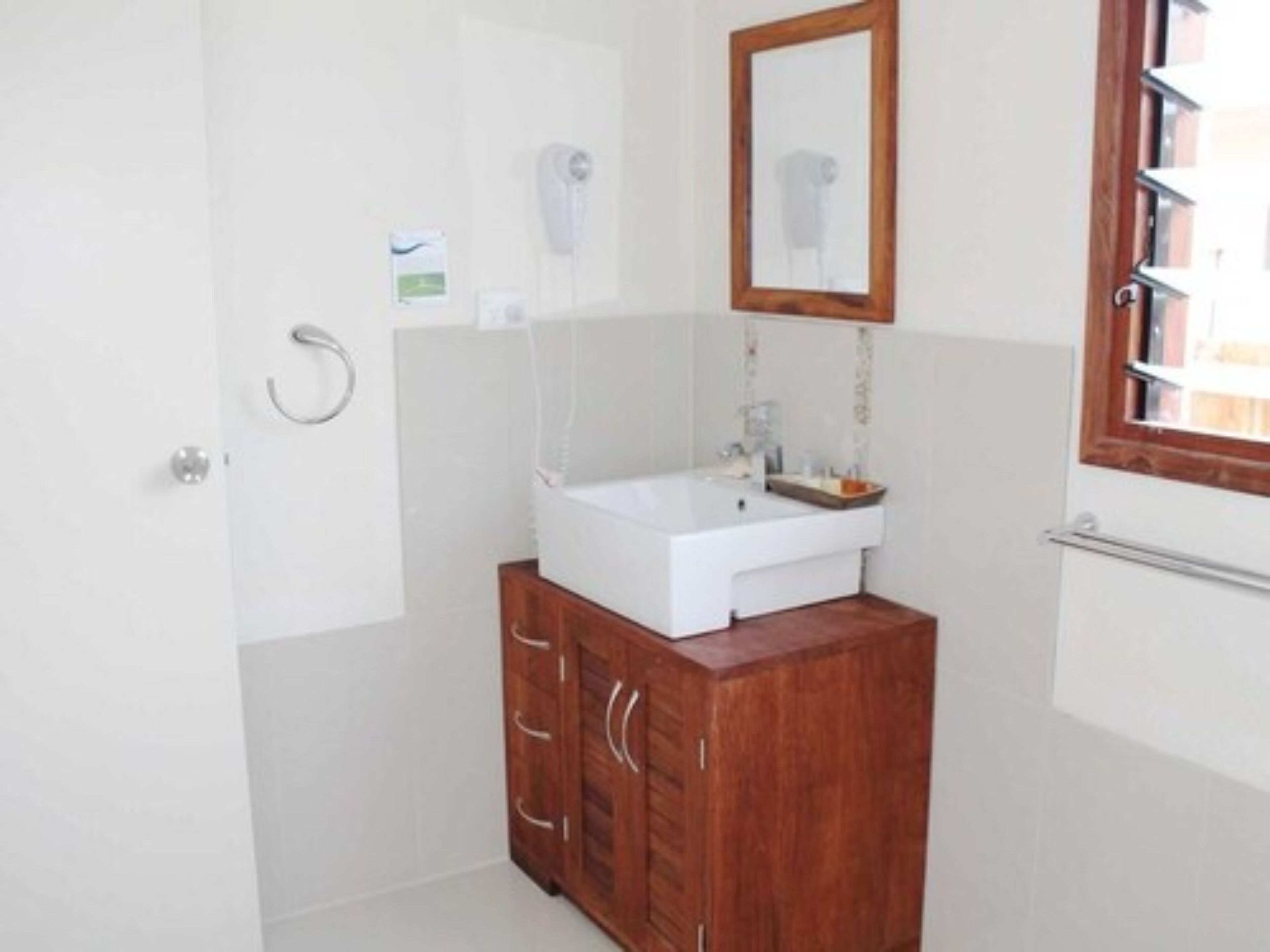 Un baño con lavamanos blanco, un mueble de madera y un espejo.