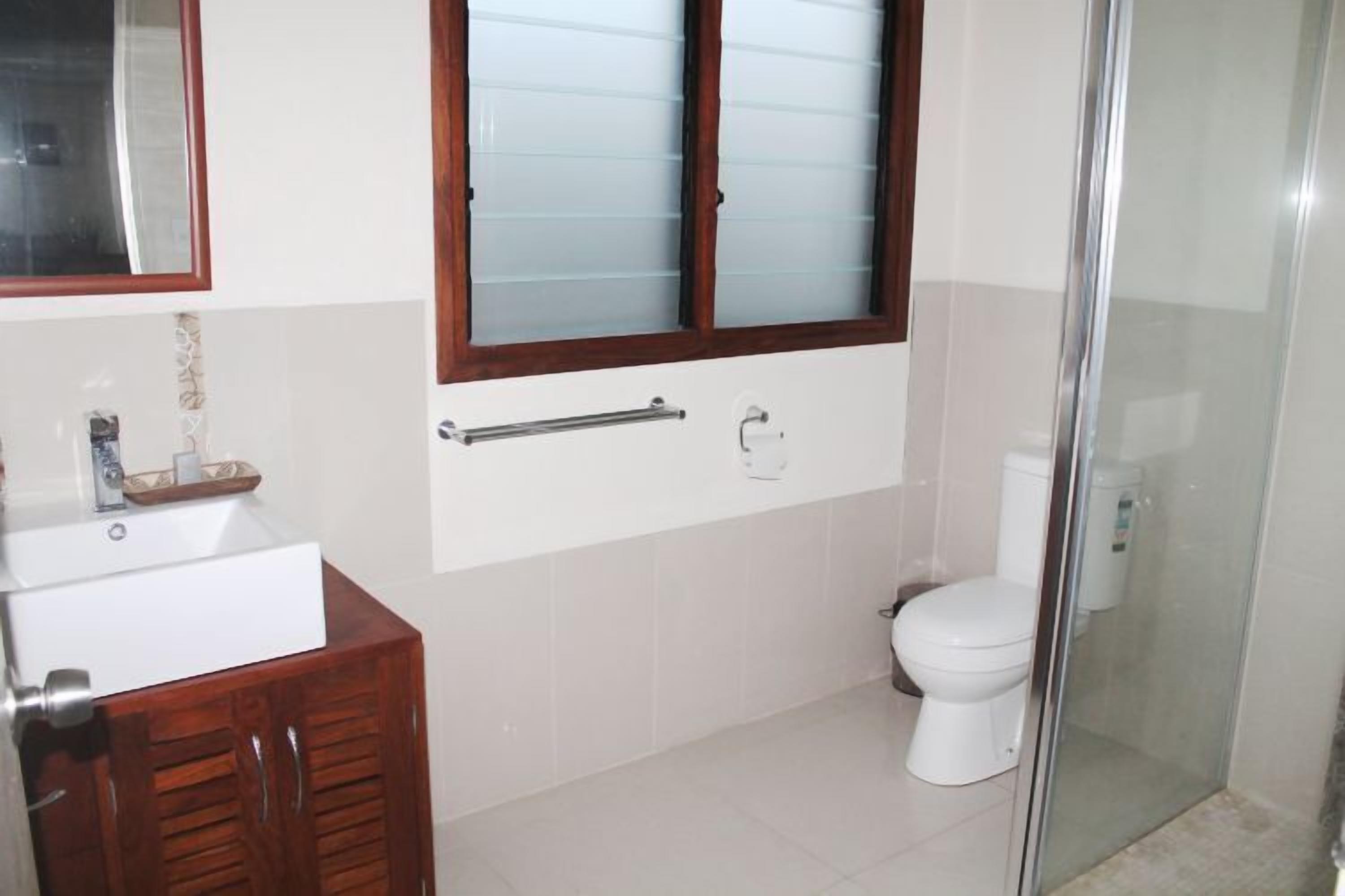 Un baño con lavamanos blanco, mueble de madera, inodoro y cabina de ducha con mampara de vidrio.