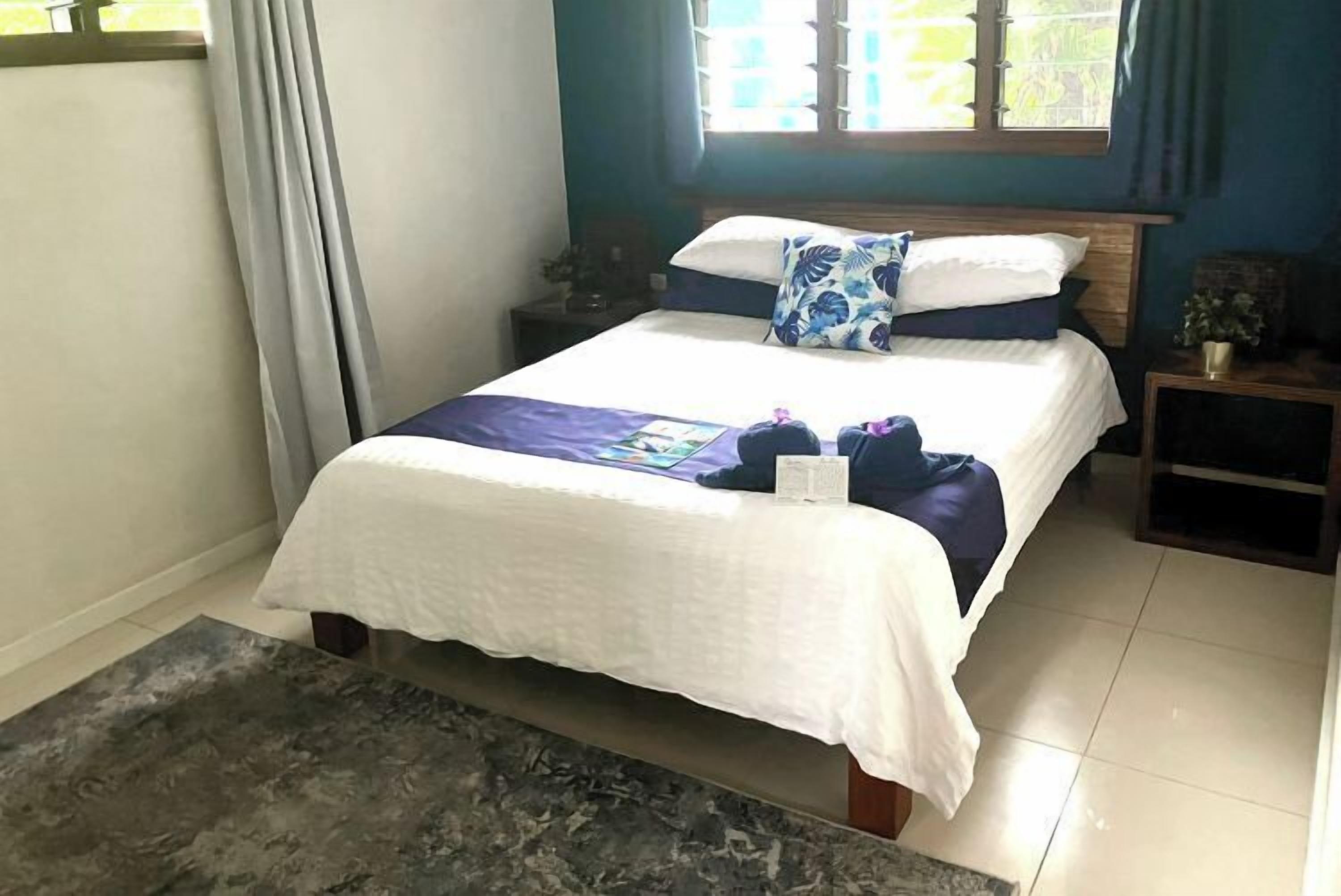 A neatly made bed with a white and blue bedspread, a wooden headboard, and a nightstand with a lamp and a small plant.