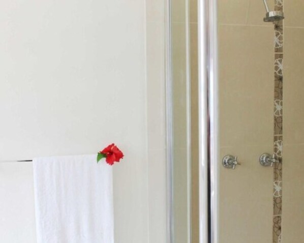 A bathroom with a glass shower enclosure, a white towel hanging on the wall, and a red flower decoration. - Vanuatu Beachfront Apartments (Mele)