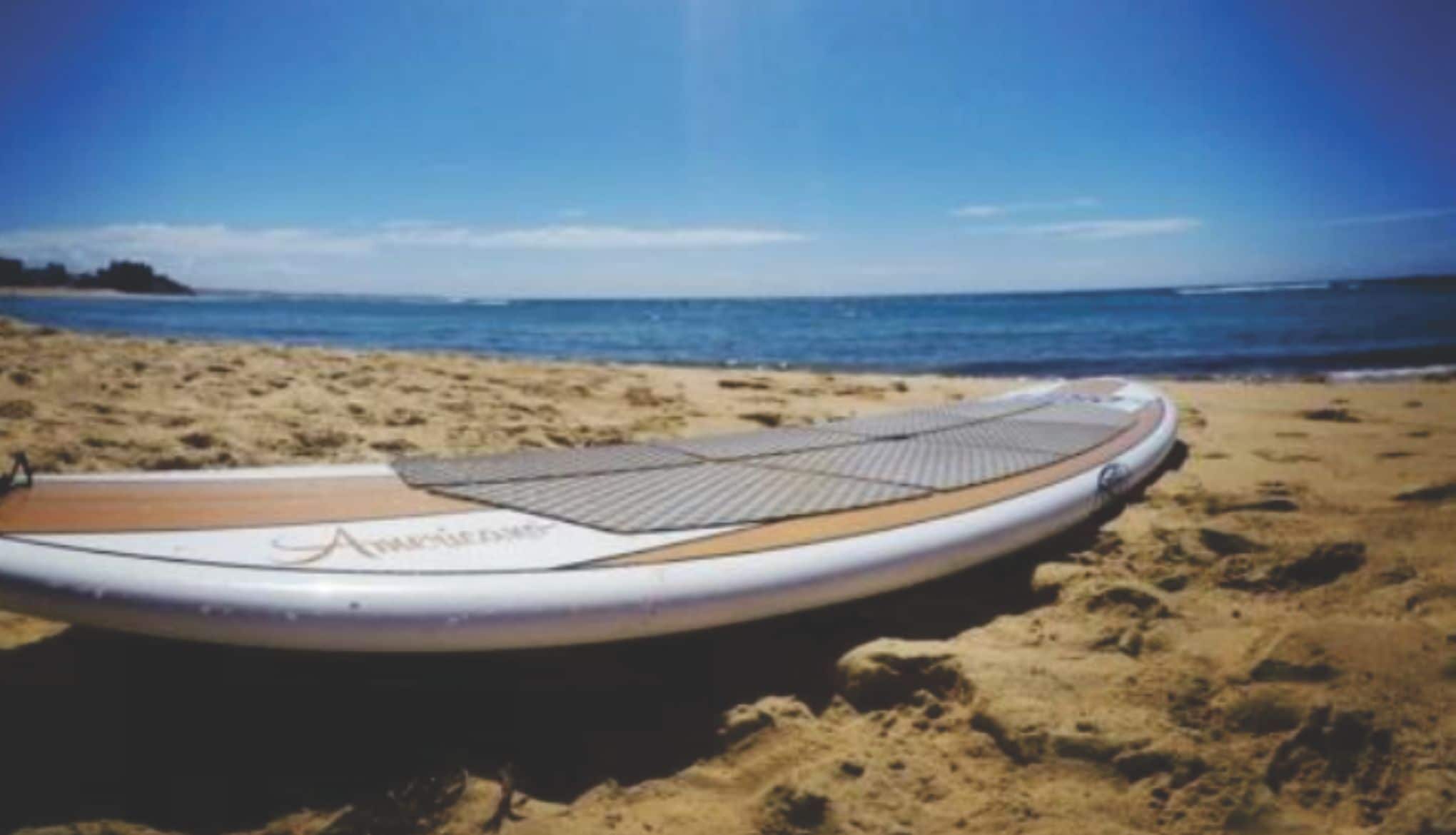 A surfboard on a sandy beach with a clear sky.
