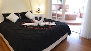 A neatly made bed with a black bedspread and white pillows, a bedside table with a clock, and a view of an outdoor patio area. - Lakeside Cottage (Kilsyth South)