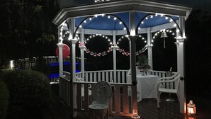 A gazebo with white railings and a blue roof, adorned with string lights and a garland. - Lakeside Cottage (Kilsyth South)