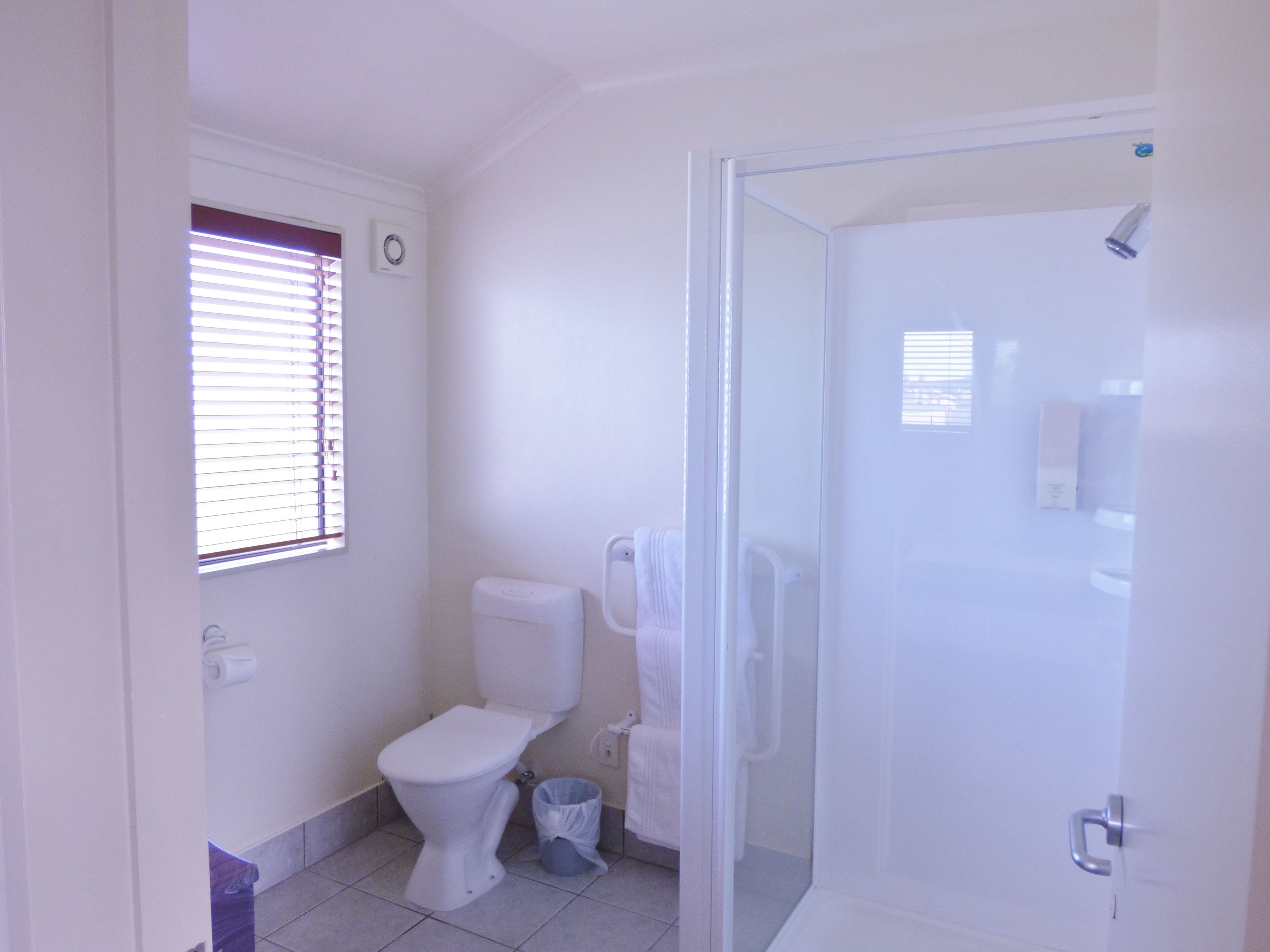 A bathroom with a toilet, a shower enclosure, and a window with blinds.