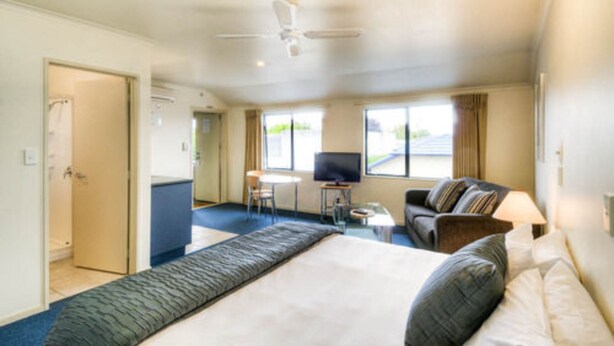 A hotel room with a large bed, a sofa, a TV, and a desk. - Claremonte Motor Lodge (Hastings)