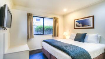 Habitación de hotel con cama, televisión, ventana con cortinas, un cuadro en la pared y lámpara.