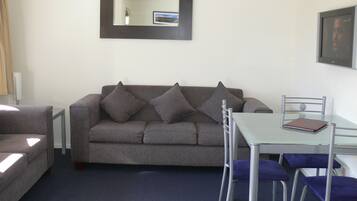 A living room with a grey sofa, a glass table, and matching chairs.
