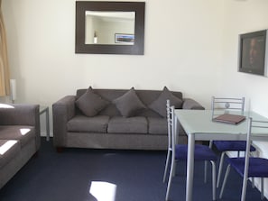 A living room with a grey sofa, a glass table, and matching chairs.