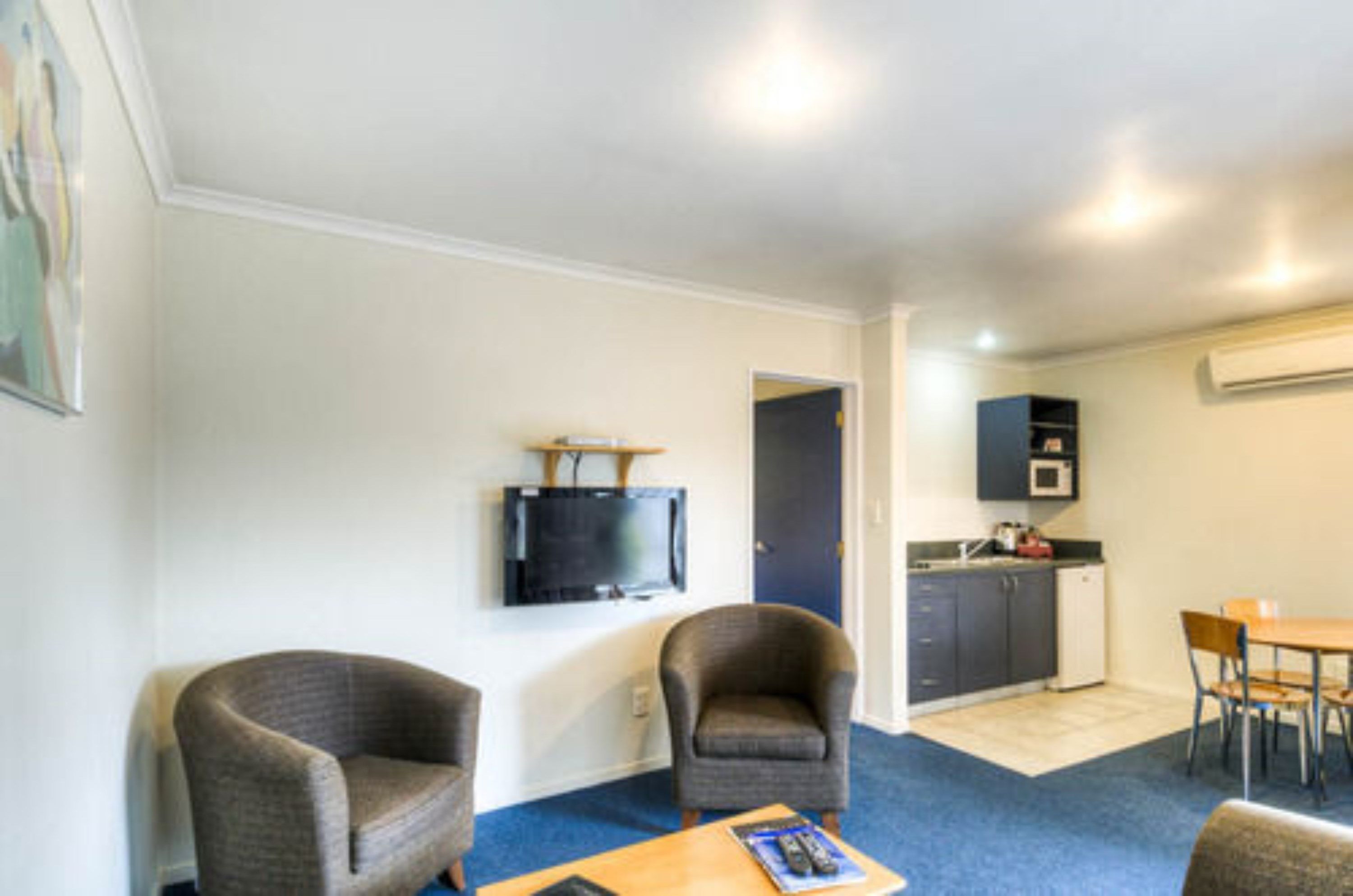 Een knus woongedeelte met een kitchenette, een wandtelevisie en twee fauteuils.
