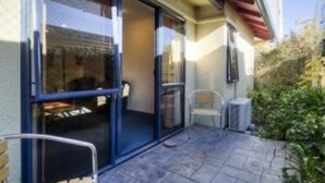 A patio with a glass door leading to a room, a chair, and a small table. - Claremonte Motor Lodge (Hastings)