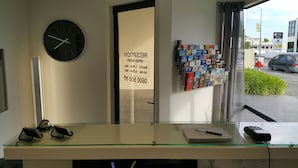 A reception desk with a clock, a bulletin board with pamphlets, and a view of the street outside. - Claremonte Motor Lodge (Hastings)