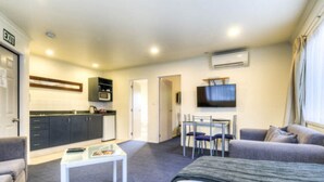 A compact hotel room with a kitchenette, a dining area, a sofa, and a TV. - Claremonte Motor Lodge (Hastings)