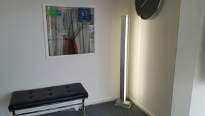 A hallway with a bench, a wall-mounted clock, and a poster with a number '9.1'. - Claremonte Motor Lodge (Hastings)