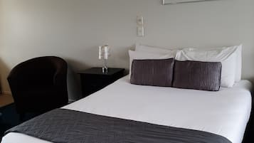 A hotel room with a large bed, a nightstand, a lamp, a chair, and a painting on the wall.