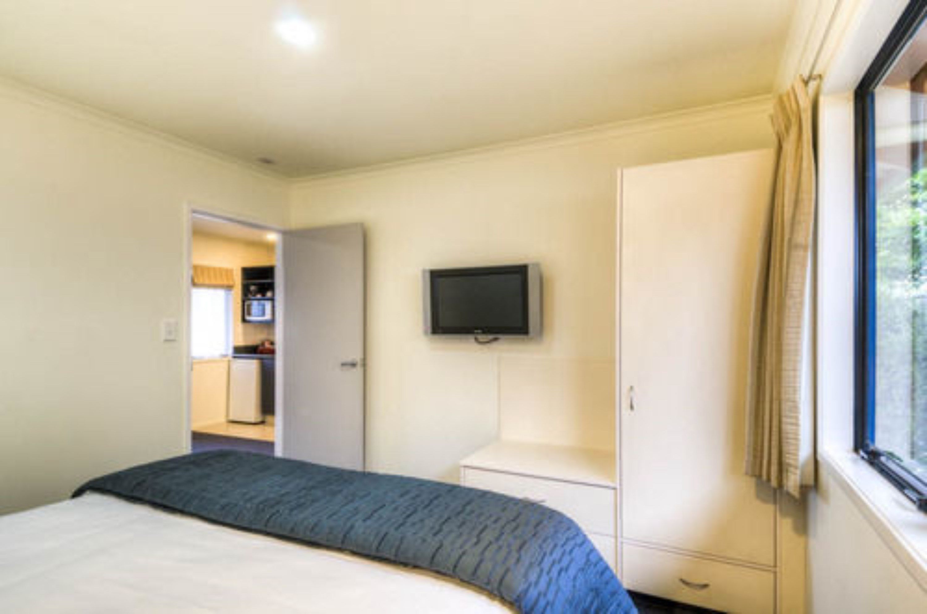 A bedroom with a bed, a television mounted on the wall, a wardrobe, and a window with curtains.