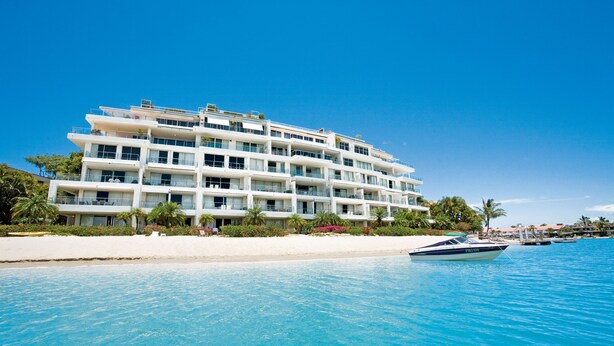 Et hotel med flere etager, altaner, en pool og udsigt til stranden.