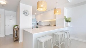 Et moderne køkken med en central ø, hvide barstole og hængende lamper.
