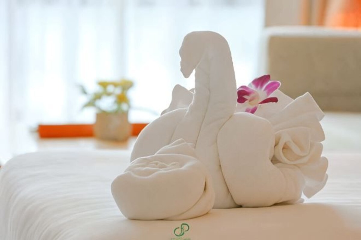 Una cama con una toalla doblada en forma de cisne y una sola flor.