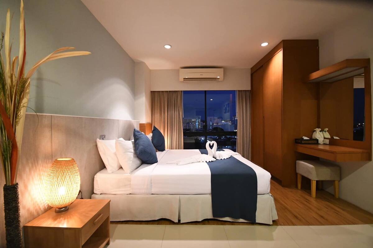 Habitación de hotel con cama, mesita de noche y vista a la ciudad de noche.