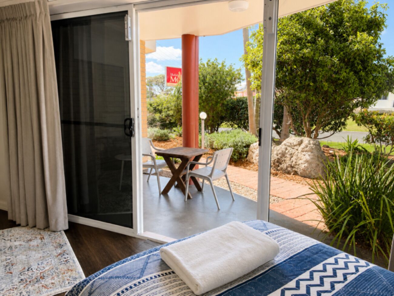 A bedroom with a bed, a sliding glass door leading to an outdoor patio with a table and chairs.