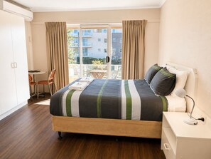 A hotel room with a bed, a desk, a chair, and a view of the outside.