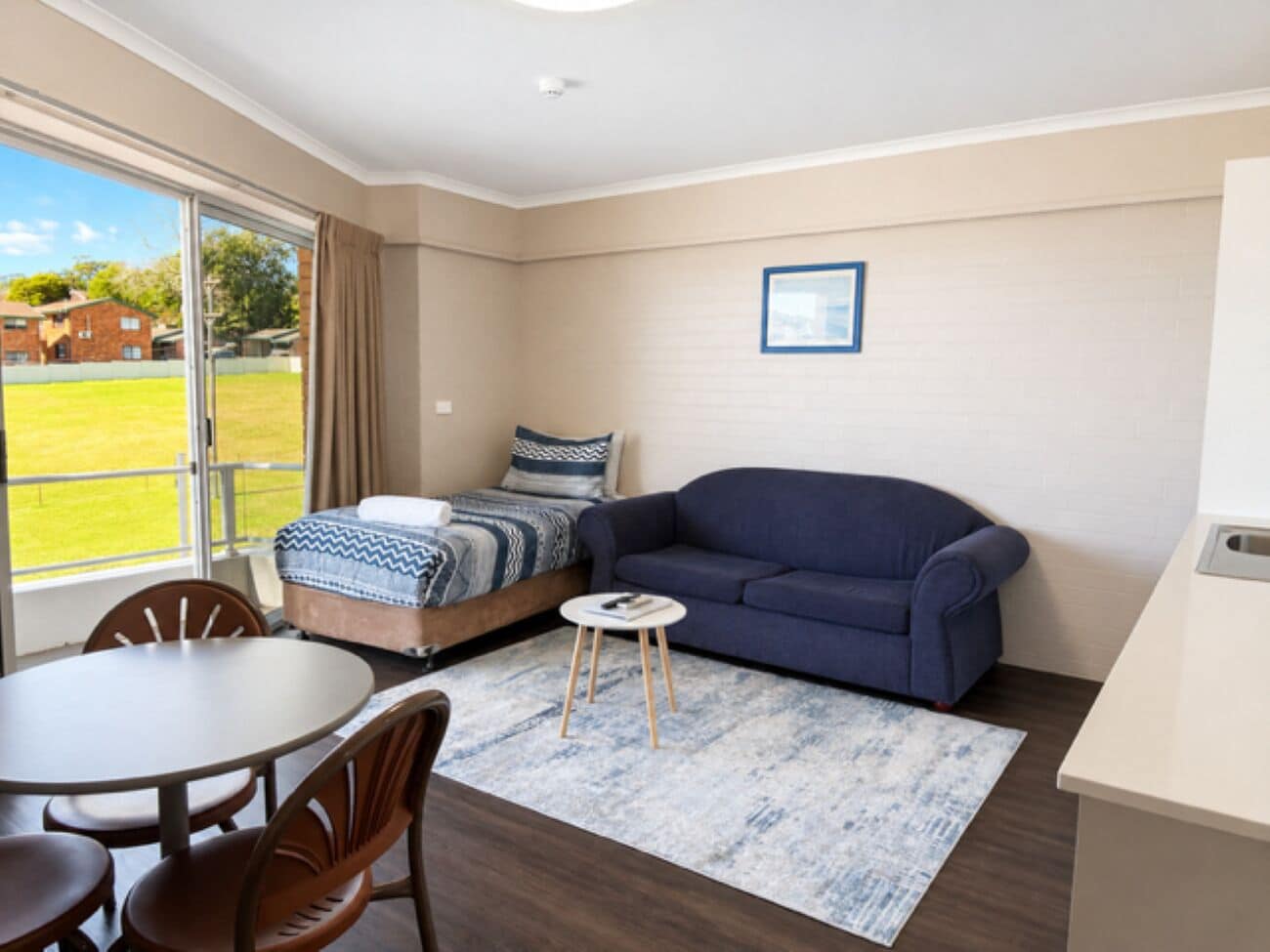 A compact room with a bed, a sofa, a dining table with chairs, and a small round table with a book.