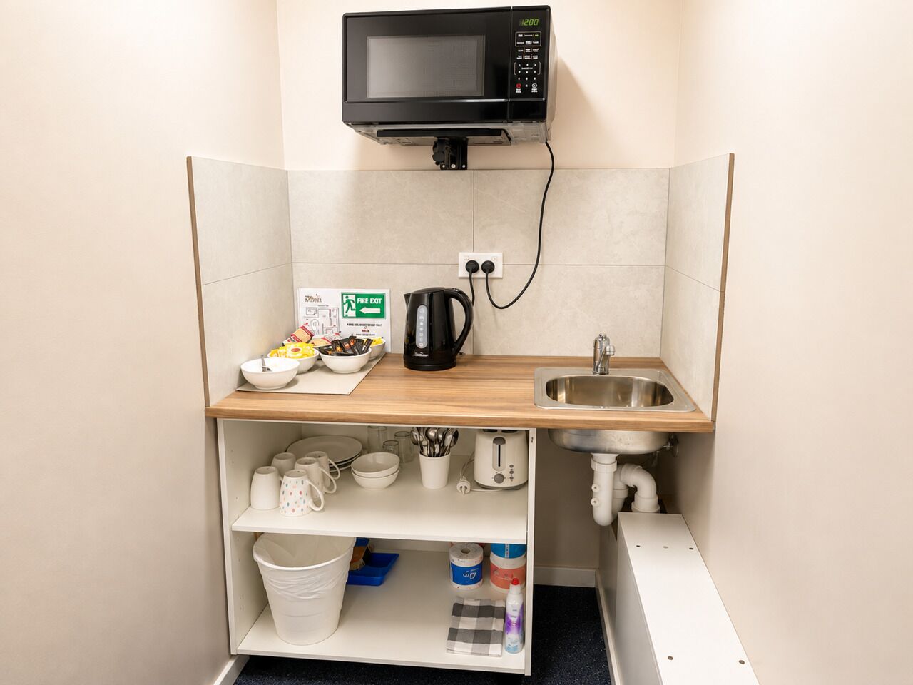 A compact kitchenette with a microwave, sink, and storage shelves.