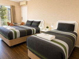 Habitación de hotel con dos camas, una mesita, una silla y un ventanal con cortinas.