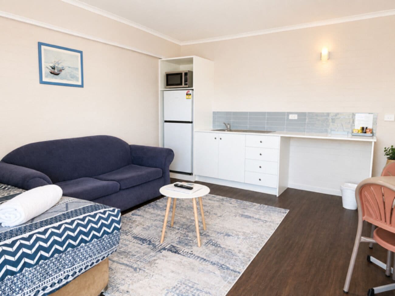 A compact living space with a sofa, a small round table, a microwave, a refrigerator, and a kitchenette area.