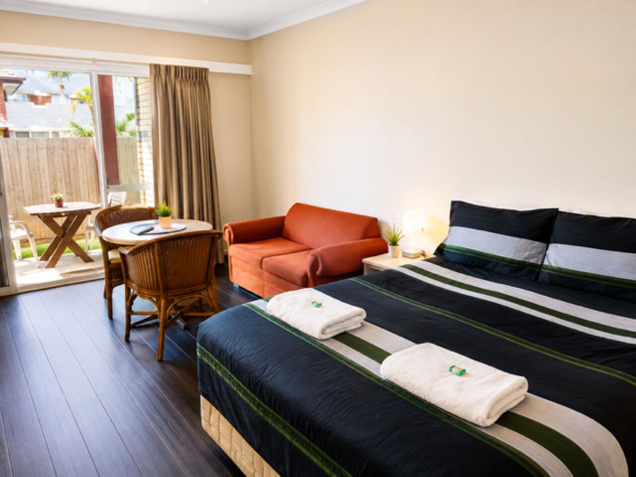 A hotel room with a bed, a chair, a table, and a view of the outdoors.