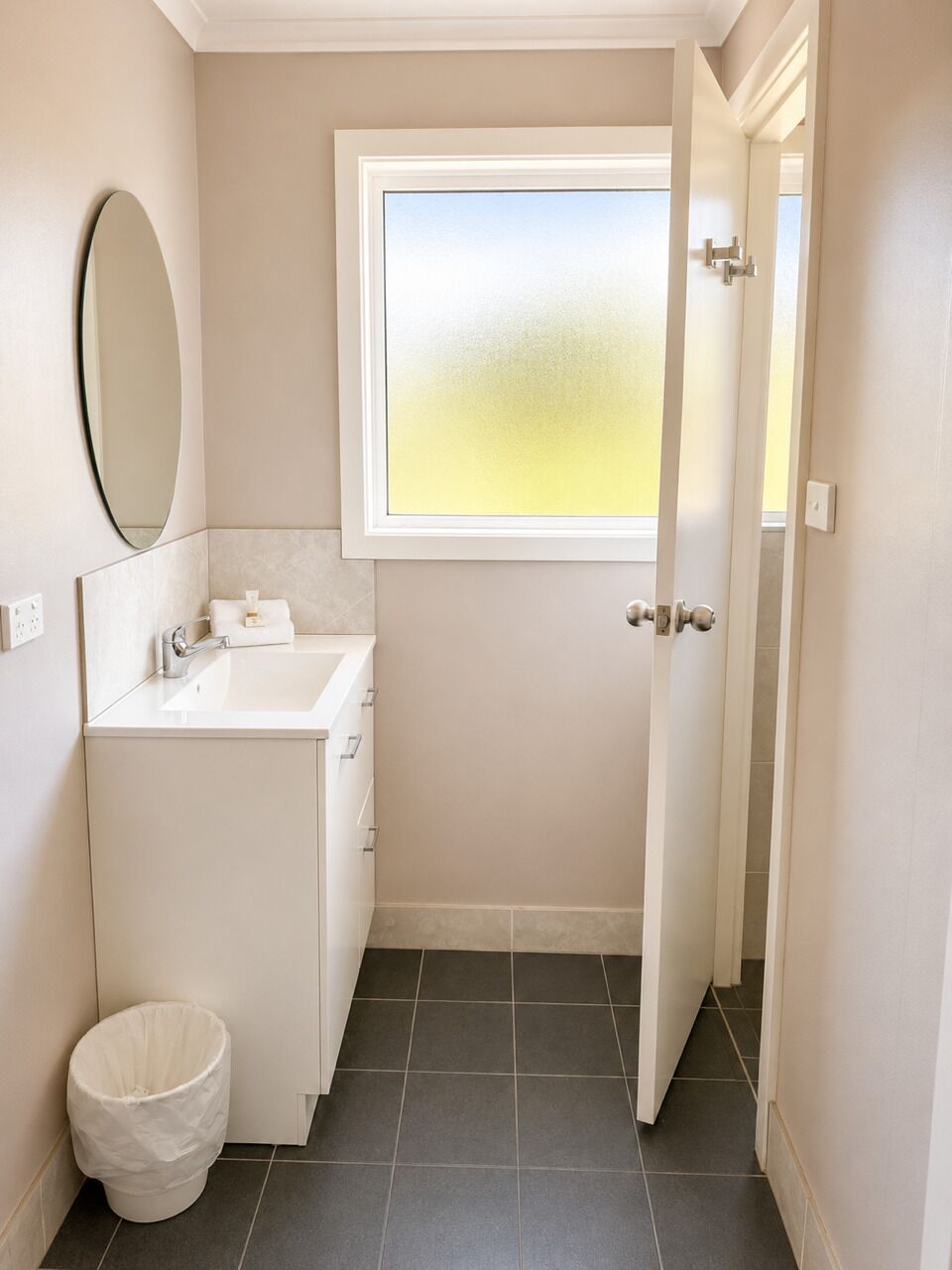 A bathroom with a white sink, a mirror, a toilet, and a window with a view.