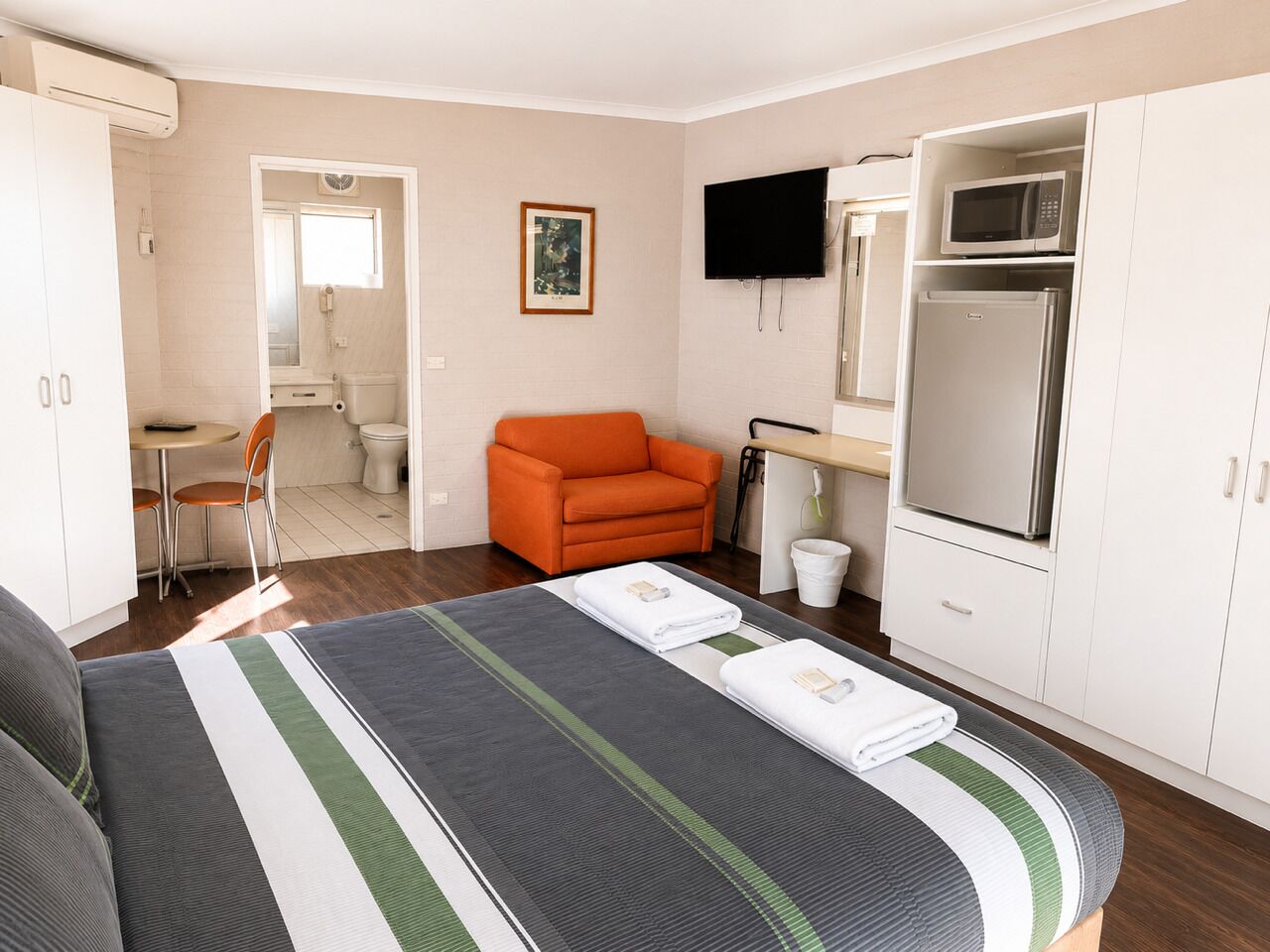 A hotel room with a bed, a chair, a TV, a microwave, and a refrigerator.