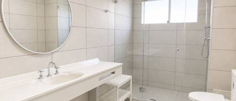 Un baño moderno con un espejo grande, un lavabo, una ducha y un inodoro.