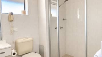 Casa de banho com sanita, chuveiro com parede de vidro e lavatório branco.
