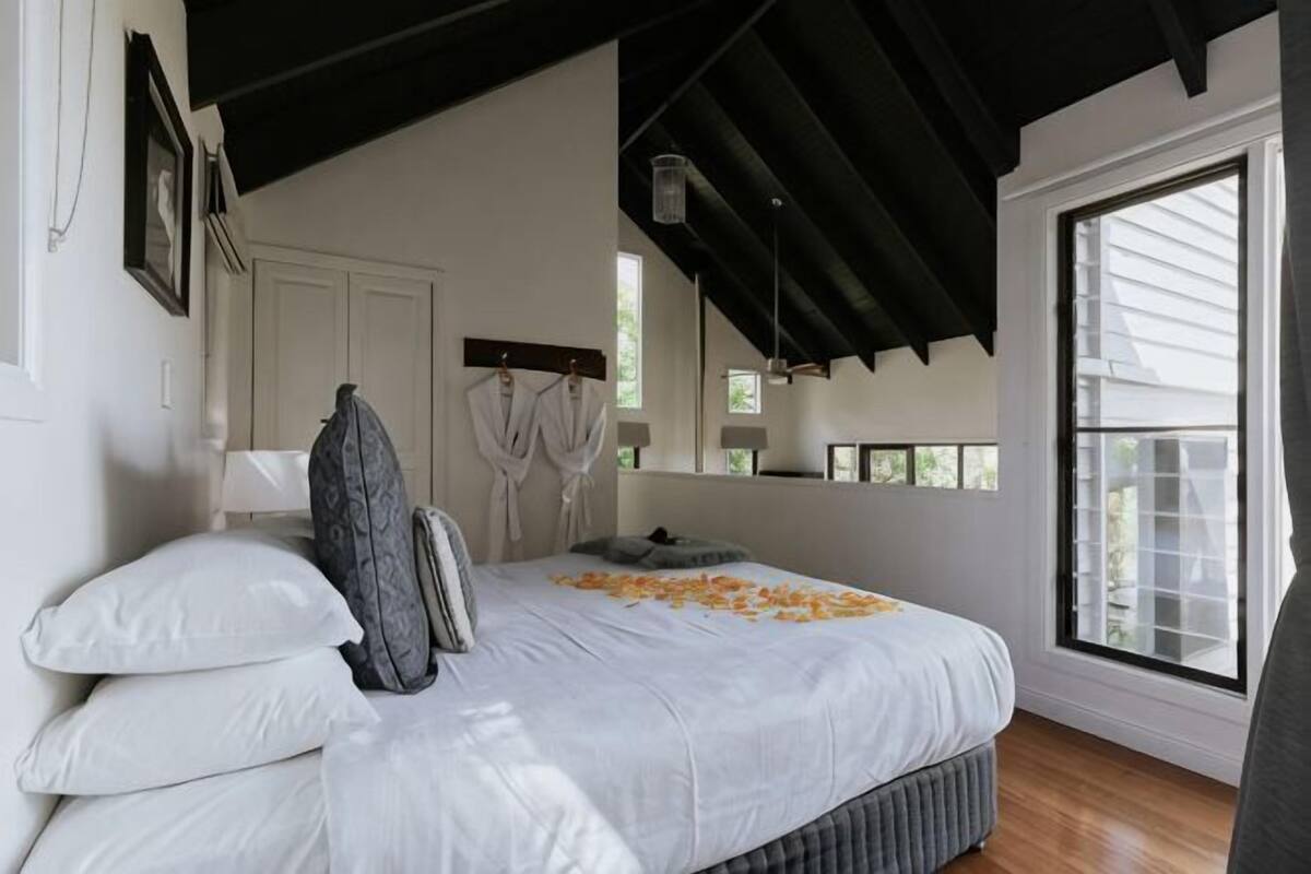 Ein Schlafzimmer mit einem großen Bett, einem Fenster mit Jalousien, einem Bademantelständer und einem Spiegel.