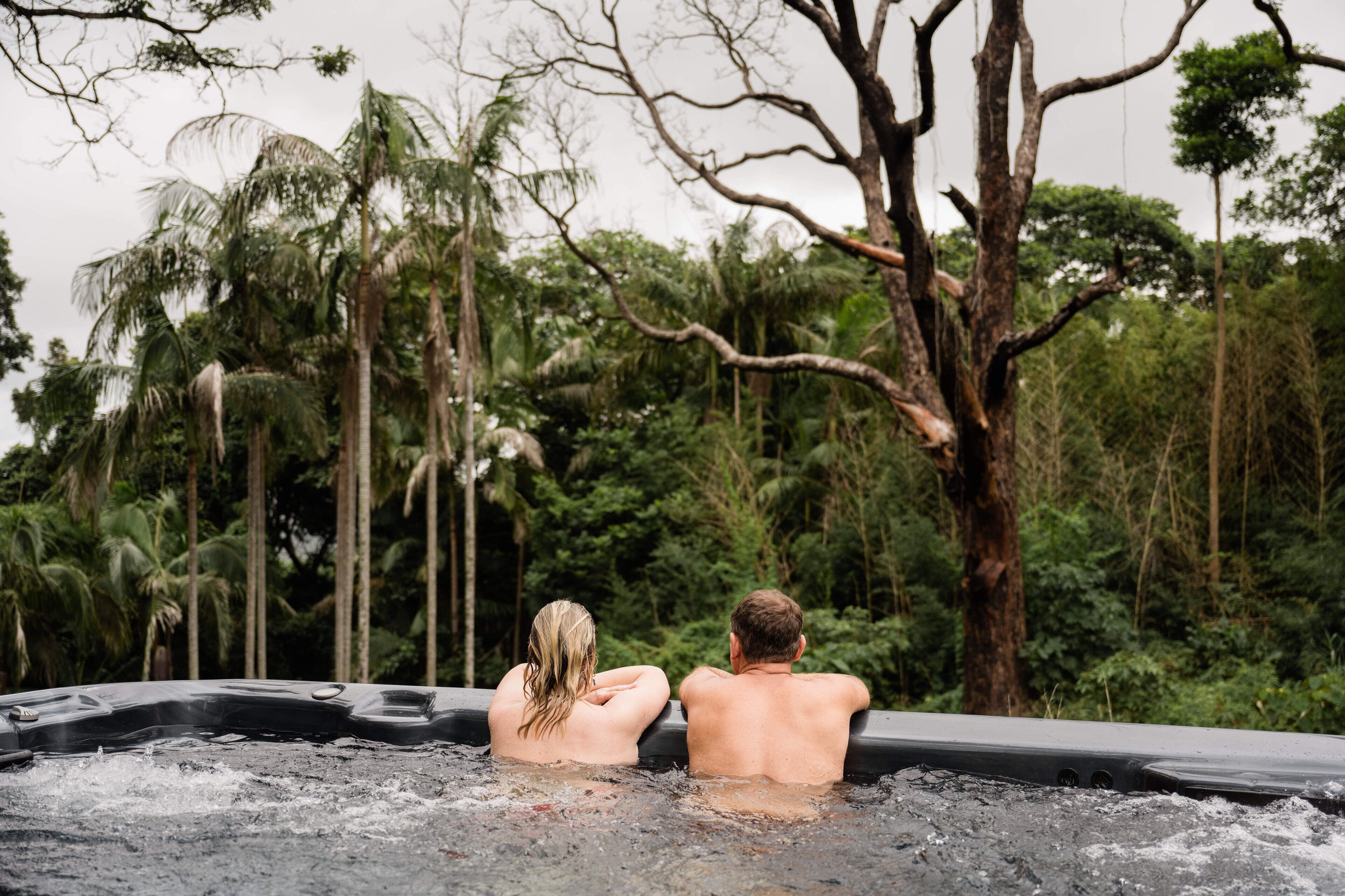 Dos personas en un jacuzzi rodeado de exuberante vegetación.