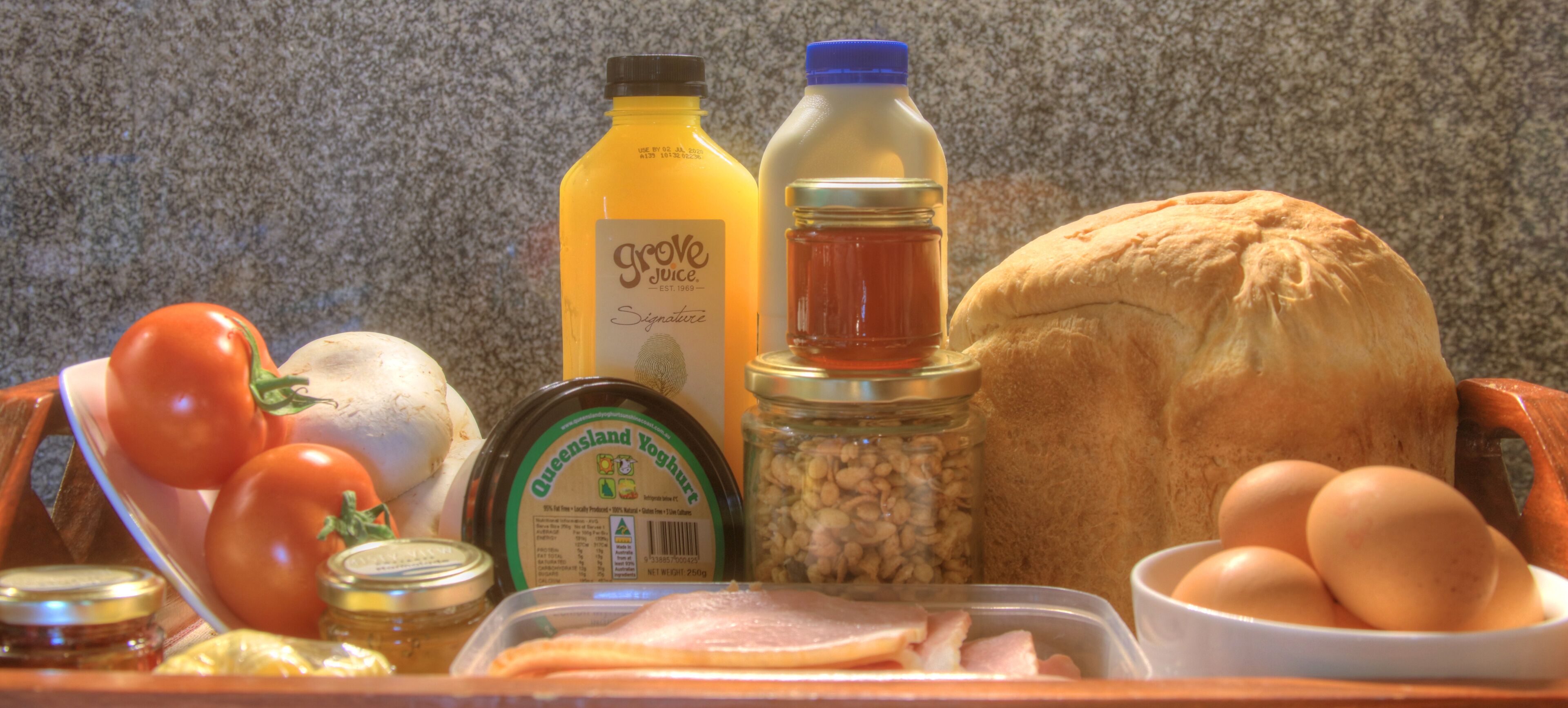 Eine Küchenarbeitsplatte mit verschiedenen Lebensmitteln, darunter Tomaten, ein Grove-Saftfläschchen, ein Honigglas, ein Brotlaib, Eier und eine Fleischpackung.