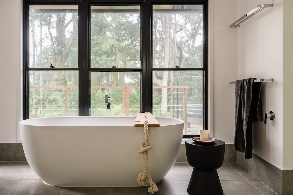 Ein modernes Badezimmer mit freistehender Badewanne, Toilette und Fenster mit Blick auf Grünflächen.
