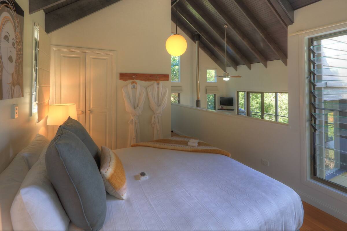 Ein Schlafzimmer mit einem großen Bett, einem Deckenventilator, einem Fernseher und einem Fenster mit Jalousien.
