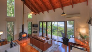 A spacious living area with a fireplace, a sofa, a television, and large windows offering a view of the outdoors. - Misty View Cottages Montville (Montville)