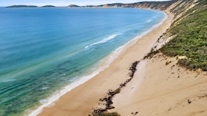 A beach with clear blue water, sandy shore, and green vegetation on the hillside.