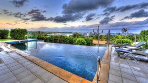 A rooftop infinity pool with a view of the ocean, surrounded by greenery and modern lounge chairs.