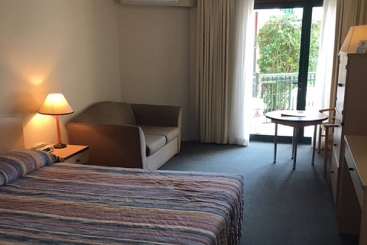 Una camera d'albergo con un letto, una scrivania, una sedia e un balcone.