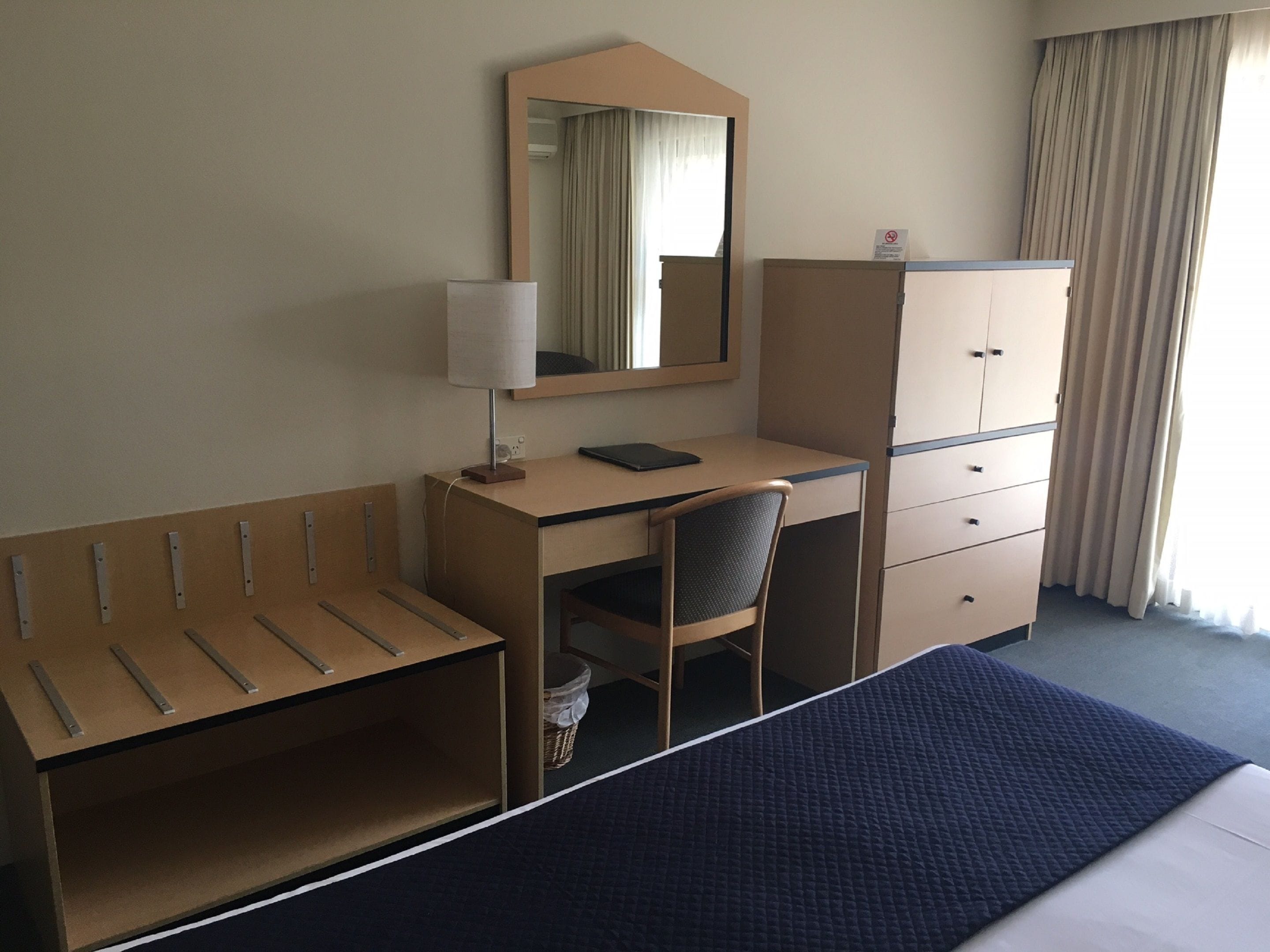 A hotel room with a bed, a desk, a chair, a wardrobe, and a mirror.