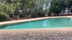 Una piscina con plataforma de baldosas de piedra y dos sillones de descanso.